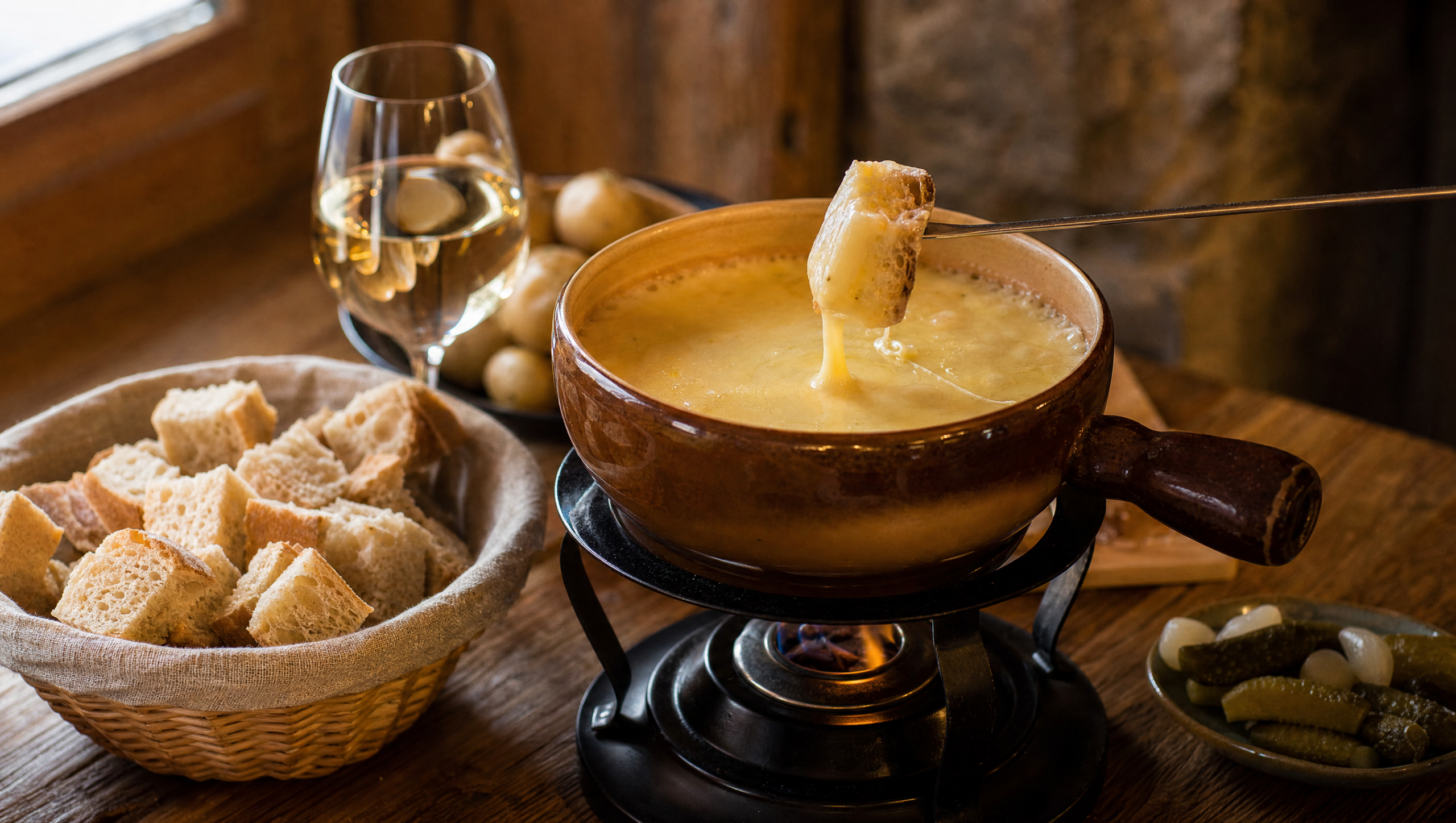 Authentic Swiss cheese fondue with melted Gruyère and Vacherin in a caquelon, bread cube on a fondue fork